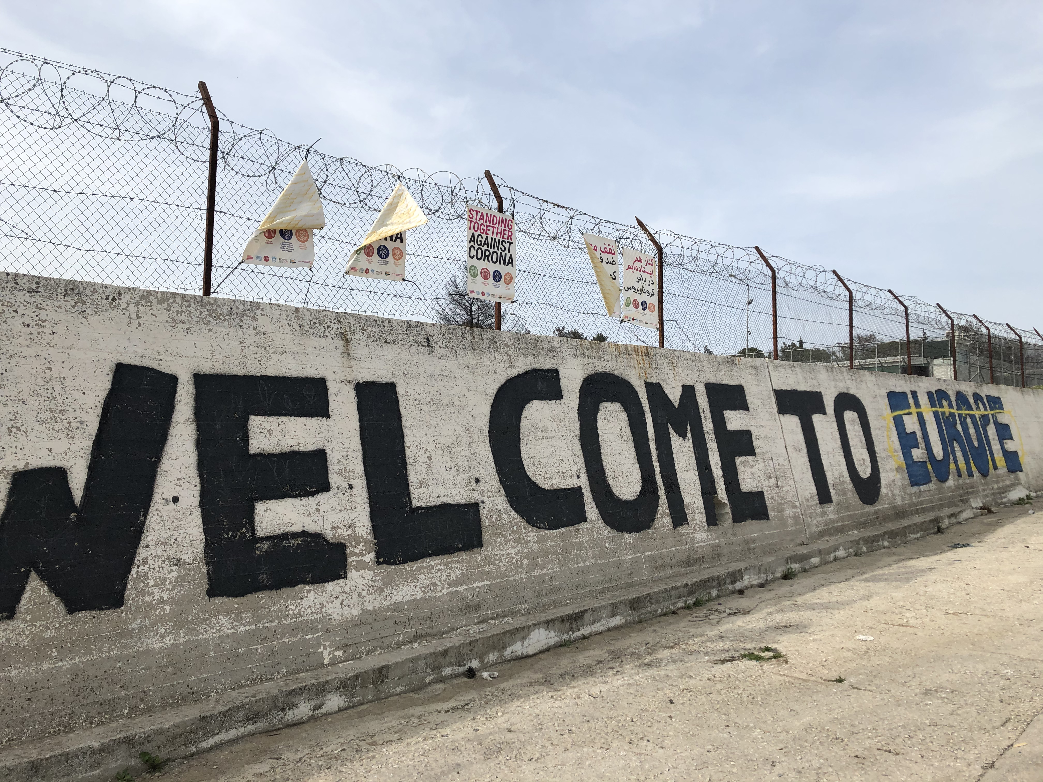 picture of a wall with barbed wire and a raffiti that says 'welcome to europe' 