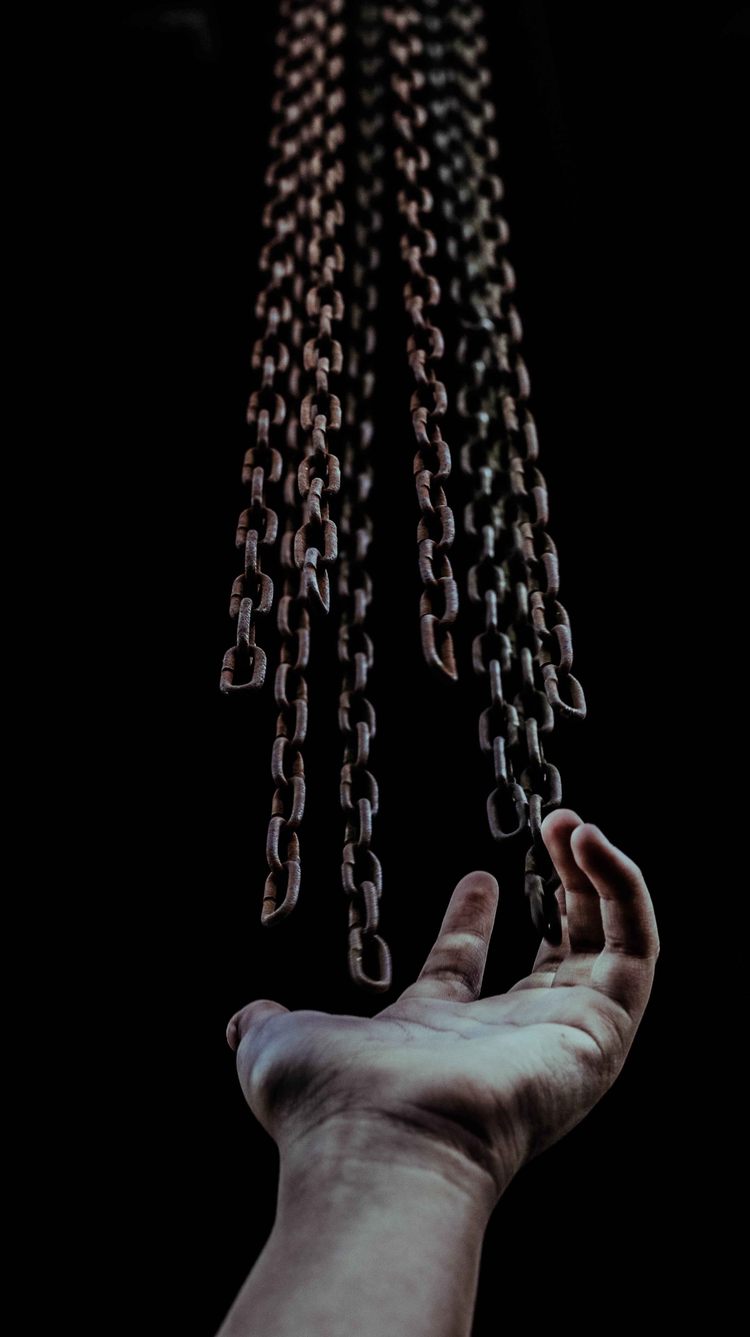 picture of a hand open with the palm towards a series of chains coming from the top of the image, over a black background 