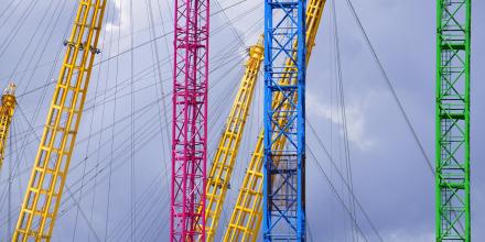 An image showing pink, yellow, and green metal bars and cables in the sky photographed from a low angle.