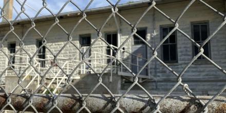 photo of a detention centre seen through the outside fencing, which is foregrounded in the picture