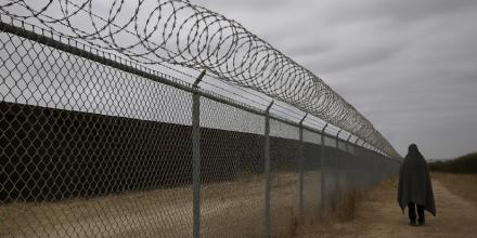 picture of a person seen from behind, walking next to a wired fence on a cloudy day