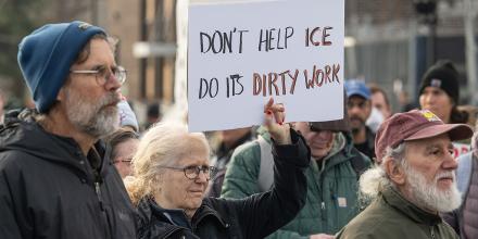 A woman holds up a sign reading 'Don't help ICE do its dirty work' standing beside other protesters 