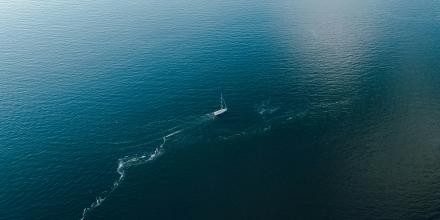 A small sailing boat seen from above in the middle of the ocean, with a line of white foam trailing out behind