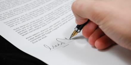 A hand signing a document with a fountain pen.