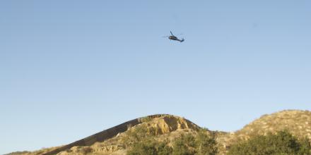A helicopter flies over a long wall snaking over scrubby green and brown hills