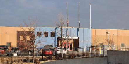 A large building with a US flag flying outside. Lettering on the outside reads: Aurora ICE Processing Center