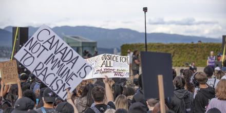 People gathered at an anti-racism protest in Vancouver. A person holds a sign reading 'Canada is not immune to racism'