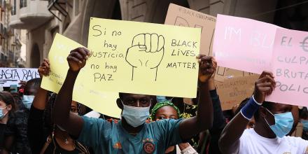 People wearing masks hold cardboard signs reading Black Lives Matter at a gathering in a city. One sign also reads: 'Si no hay justicia no hay paz'