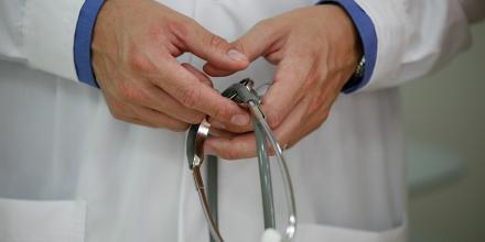 Close up of a person's hands holding a stethoscope – they wear a white lab coat