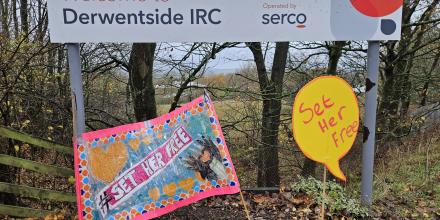 A sign reads 'Welcome to Derwentside IRC' with Serco logo. A pink protest banner has been placed below reading '#SetHerFree' with a yellow placard in speech bubble shape also reading 'Set her free' 