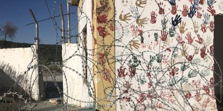 A wall covered in painted hand prints, behind barbed wire