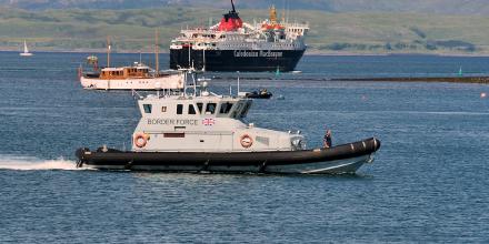 A UK border force vessel in the English Channel – a ferry and another boat pass behind it, and green hills can be seen on the shore close by