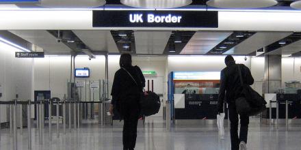 People walk through a brightly lit hall with a blue sign reading 'UK border' overhead