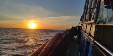 A setting sun over the wide open sea, shot from on board a rescue boat – the orange side of the boat visible on the right-hand side