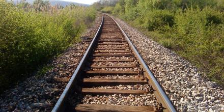 Train tracks through a countryside along the Balkan route. Green shrubs border the tracks