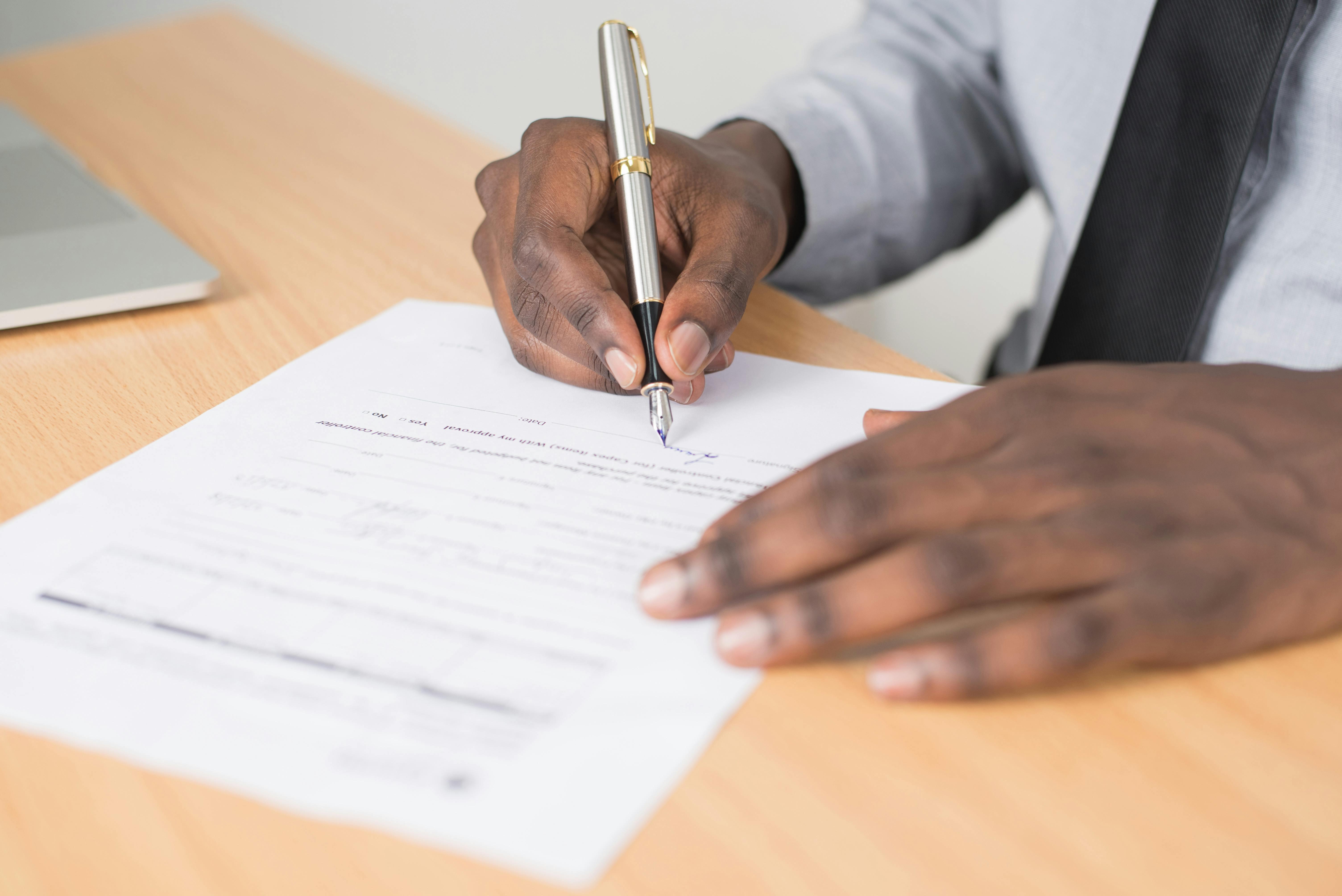A person holding a gray pen signing a contract on brown wooden table.