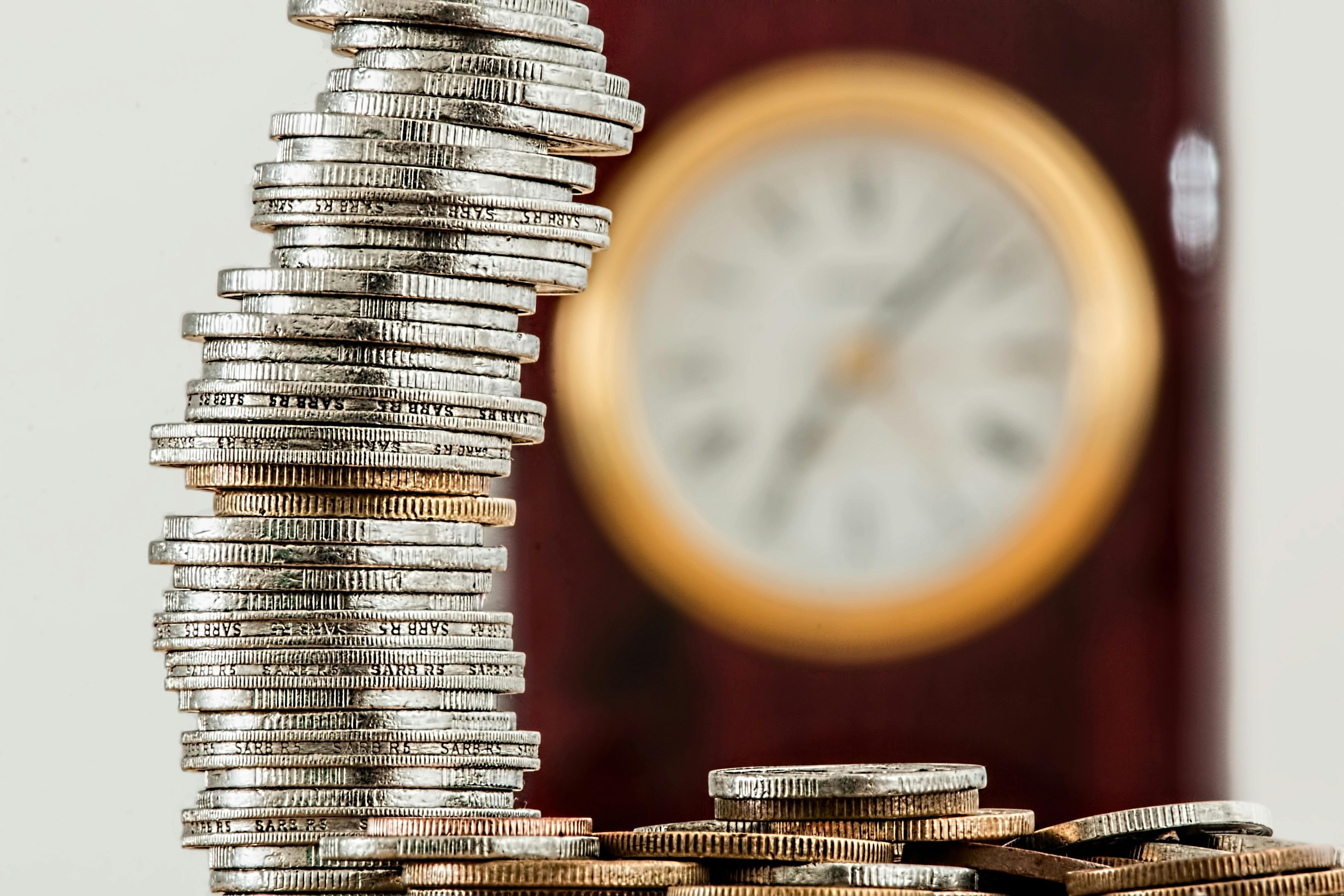 An image showing a stack of silver and gold coins in front of a blurred background showing a golden clock.