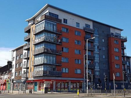 A modern building block with several storeys, balconies on the corners, and red panelled facades. 