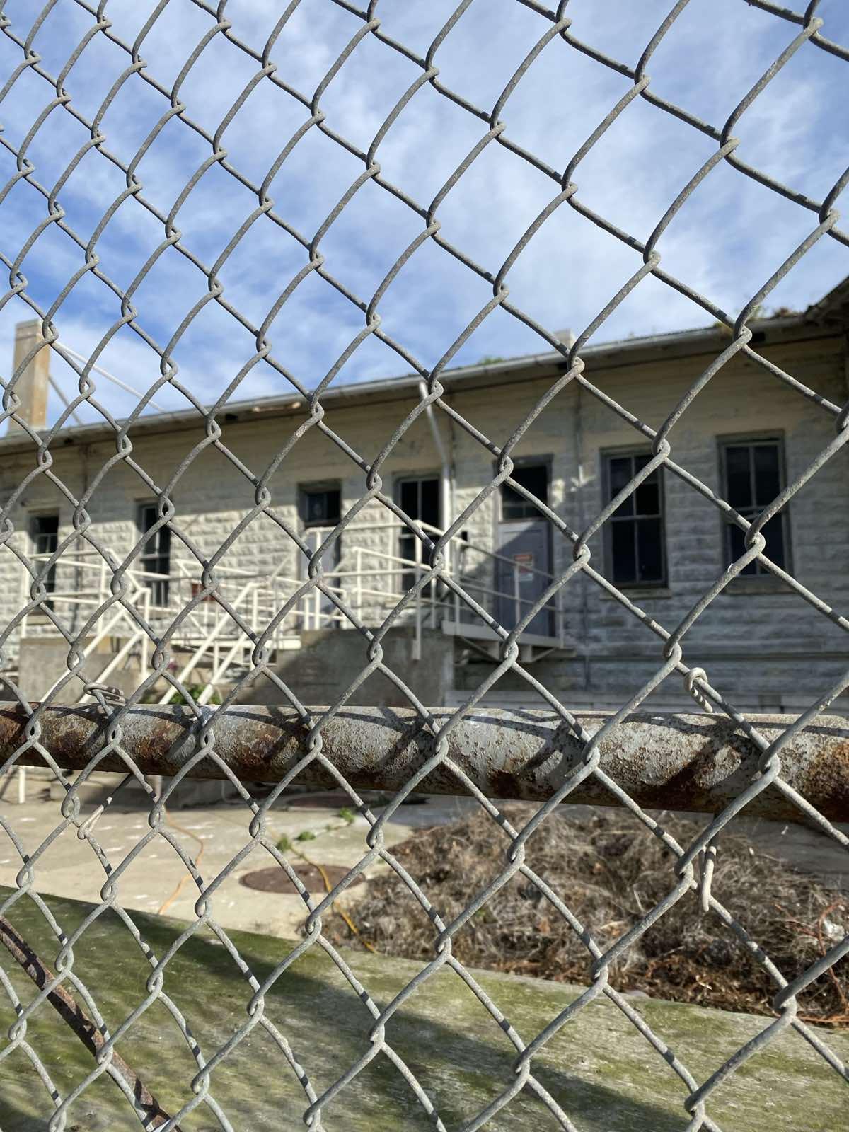 photo of a detention centre seen through the outside fencing, which is foregrounded in the picture
