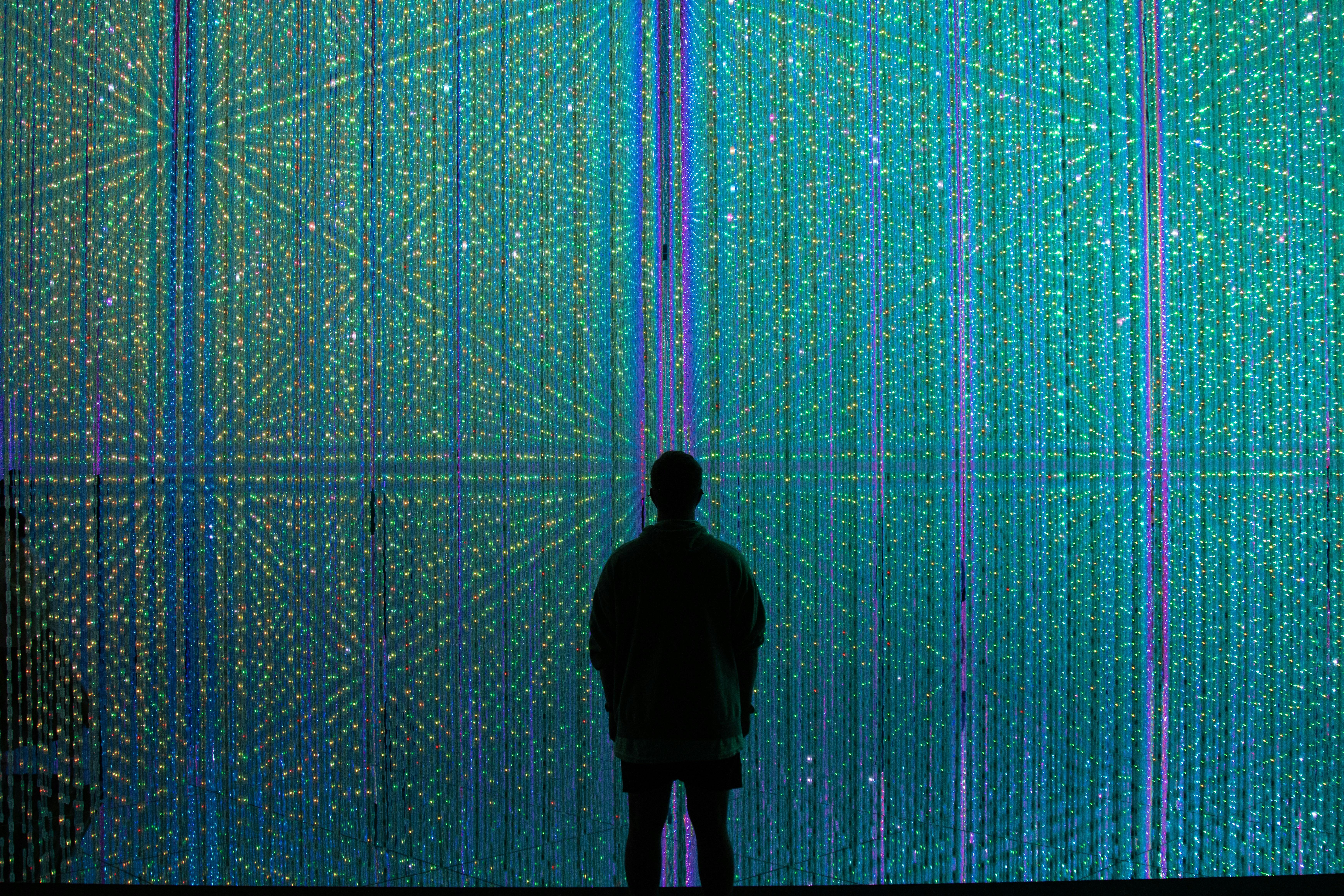 A person stands in front of a huge screen with vertical blue and purple lines of light 