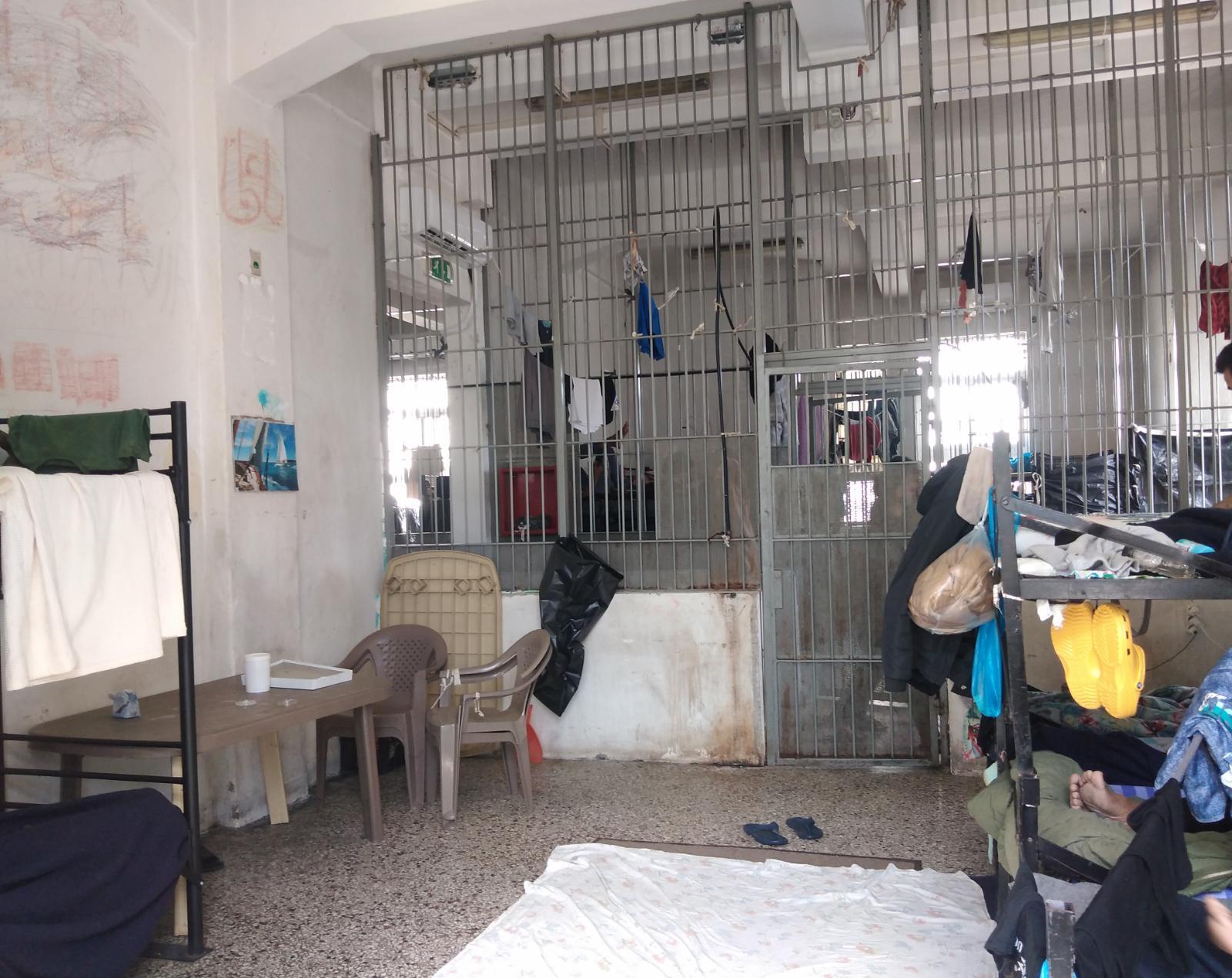 The inside of a cell in immigration detention –&nbsp;metal beds, clothes and possessions on the beds, a wall of bars to the corridor, bright overhead lights, someone's feet can be seen as they lay on the bed