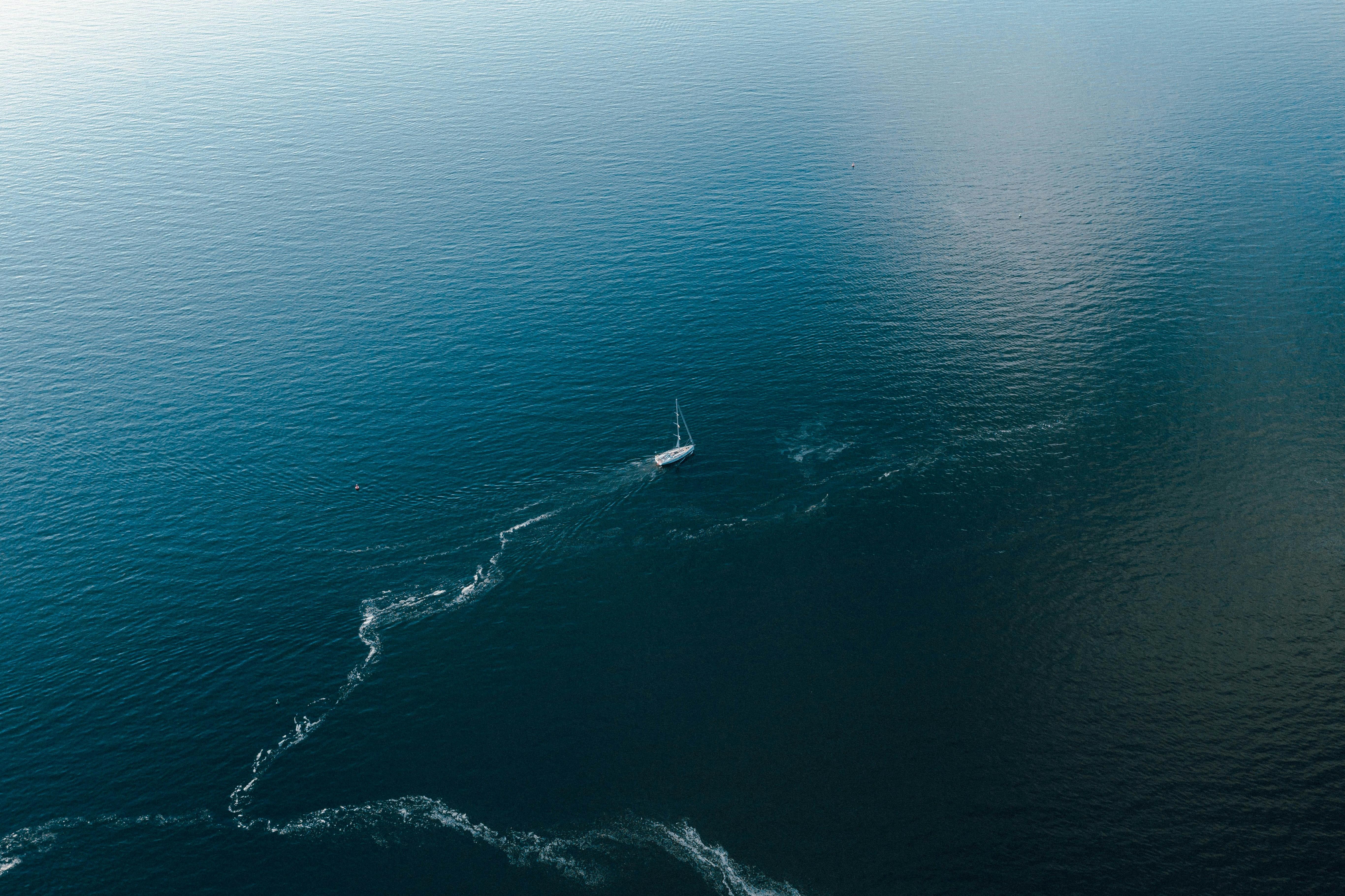 A small sailing boat seen from above in the middle of the ocean, with a line of white foam trailing out behind