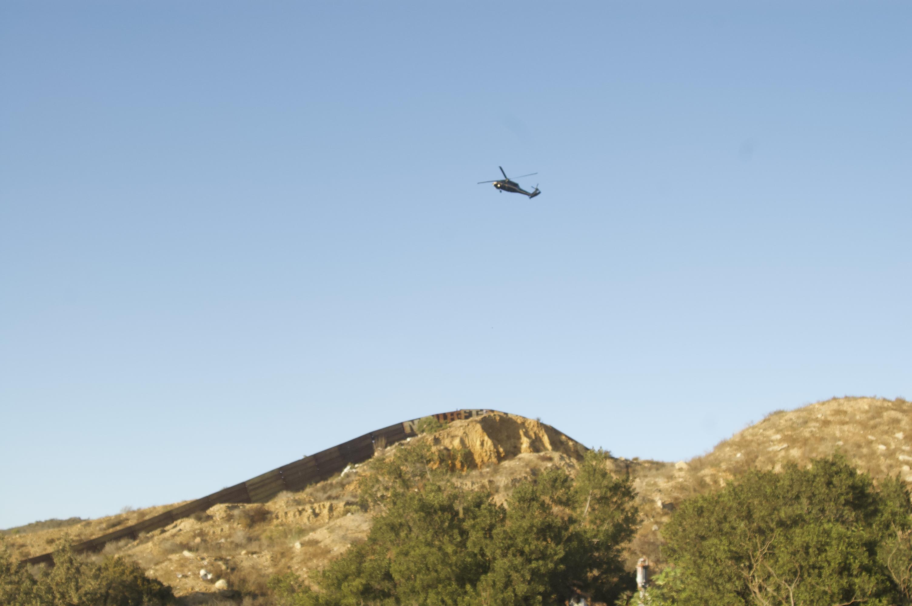 A helicopter flies over a long wall snaking over scrubby green and brown hills
