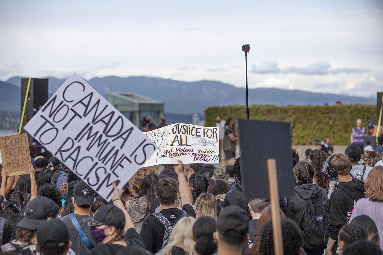 People gathered at an anti-racism protest in Vancouver. A person holds a sign reading 'Canada is not immune to racism'