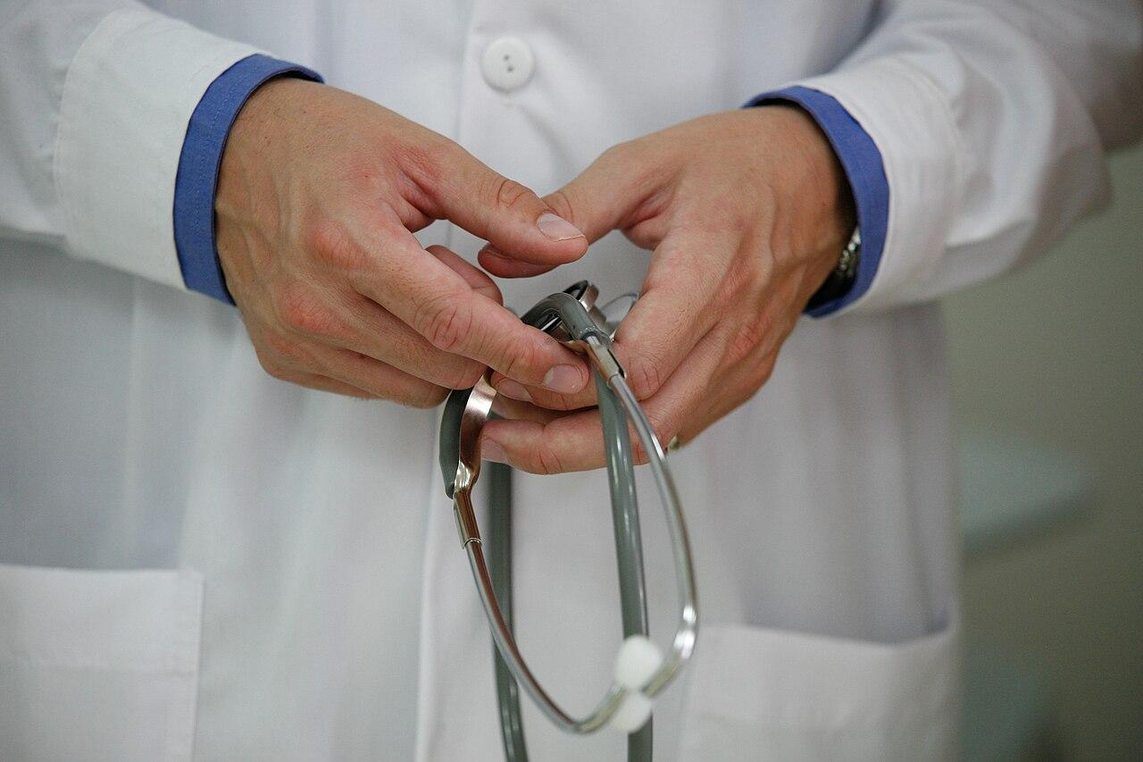 Close up of a person's hands holding a stethoscope –&nbsp;they wear a white lab coat