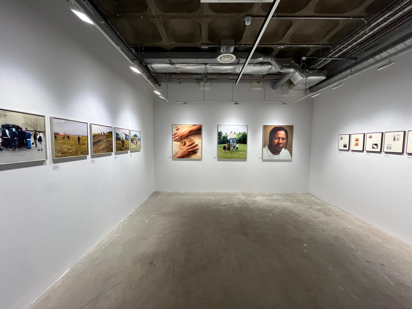 Images on a gallery wall: one shows two hands. One, a man's face
