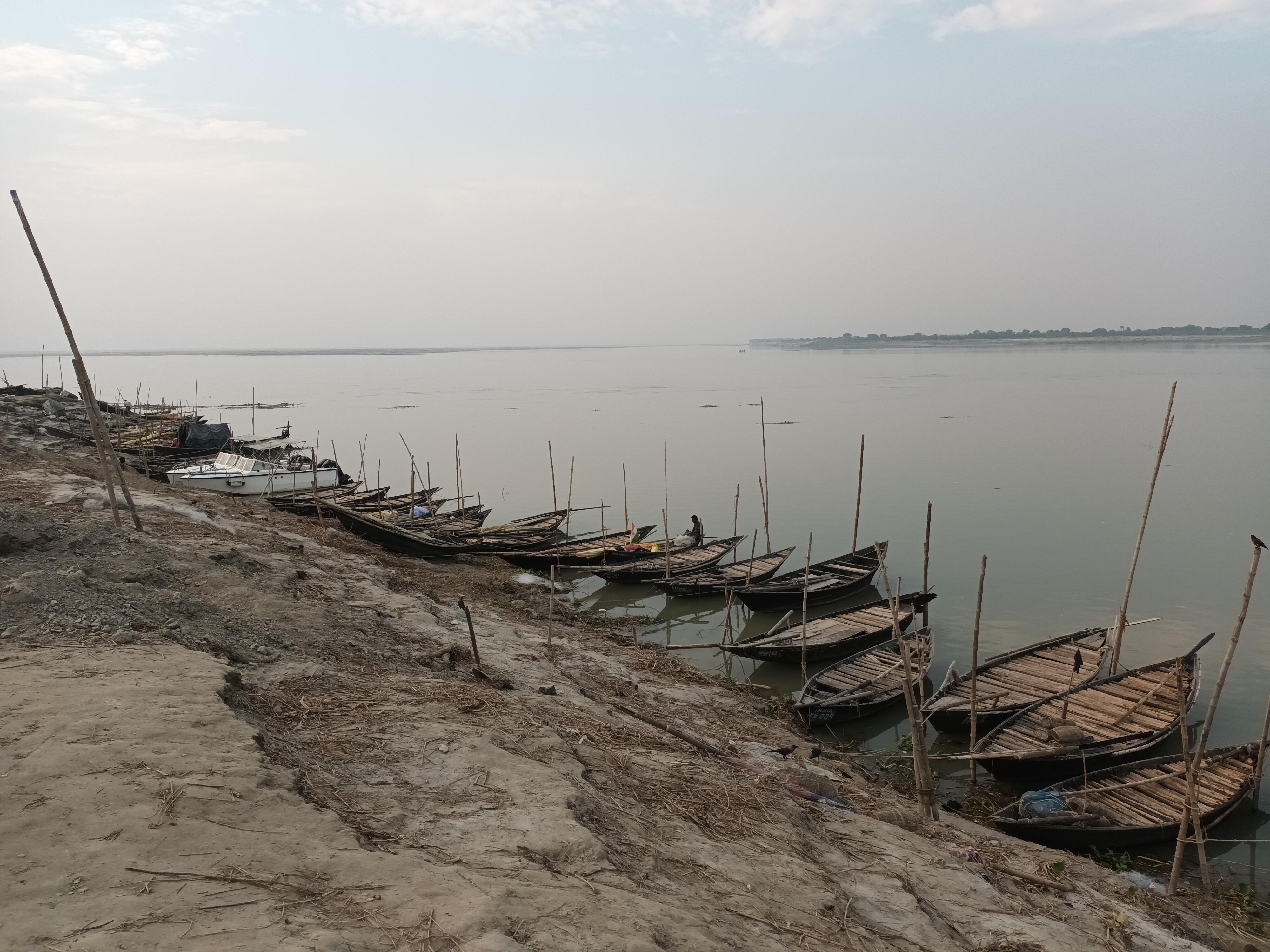 Narrow fishing boats tied up along the dusty edge of the river. The opposite bank can be seen in the far distance