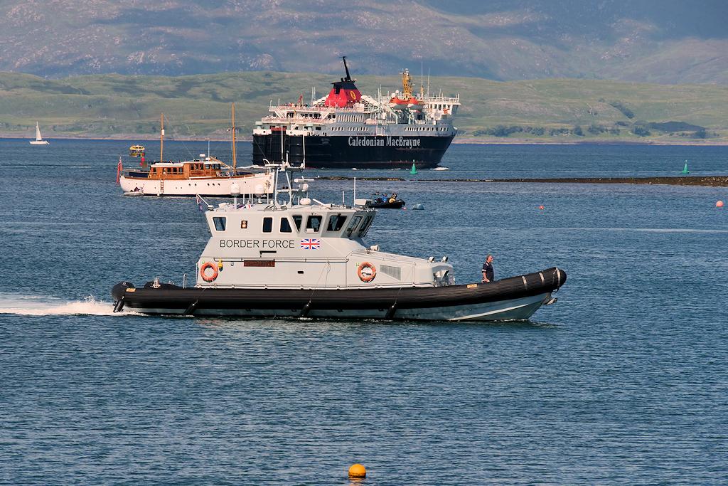 A UK border force vessel in the English Channel –&nbsp;a ferry and another boat pass behind it, and green hills can be seen on the shore close by