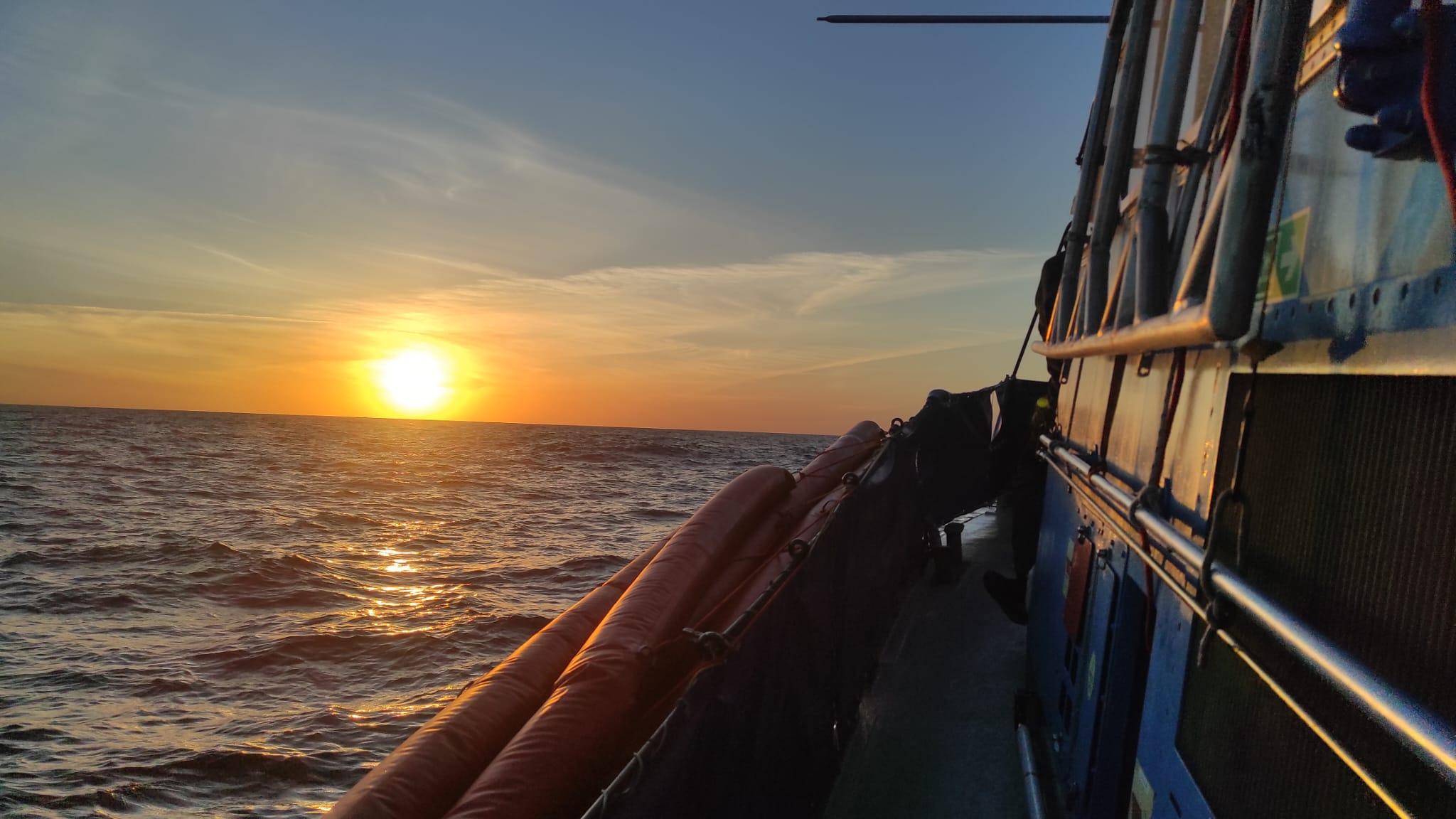 A setting sun over the wide open sea, shot from on board a rescue boat –&nbsp;the orange side of the boat visible on the right-hand side