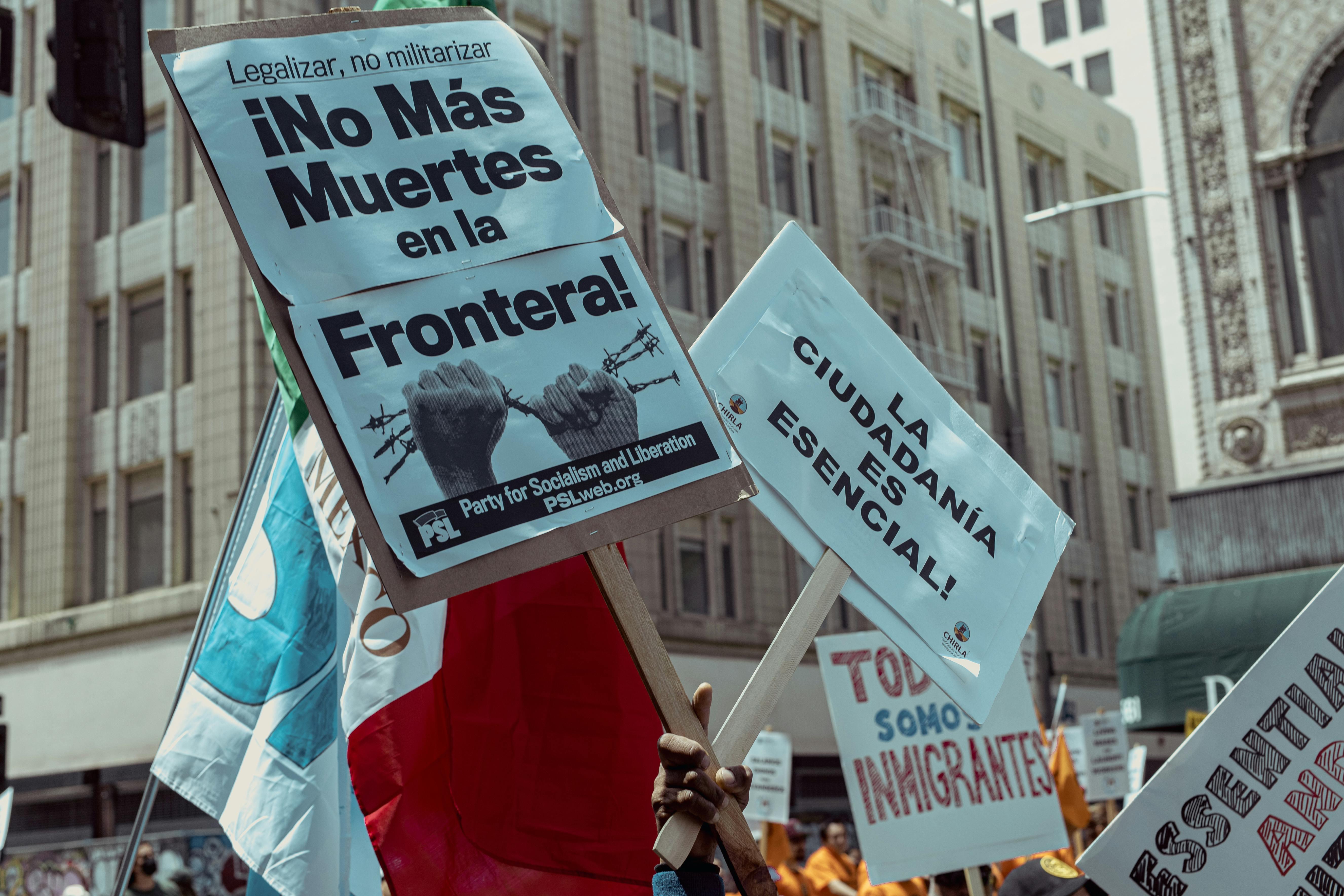 Picture of a sign that says "No Mas Muertes en la Frontera" and one that says "La Ciudadania es esencial!"